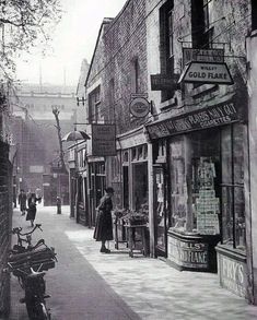 an old black and white photo of people walking down the street in front of shops