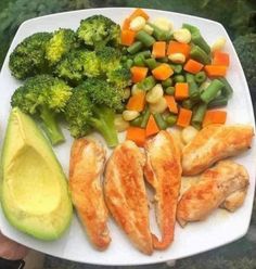 a white plate topped with chicken, broccoli and avocado next to sliced carrots