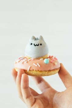 a hand holding a miniature donut with a cat on top of it and sprinkles