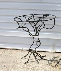 a metal table sitting on top of a sidewalk next to a white garage door with a plant growing out of it