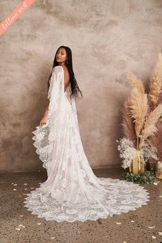 a woman standing in front of a wall wearing a white wedding dress with long sleeves