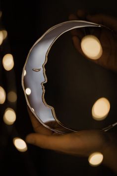 a person holding a glass object in their hand with lights around it and the moon behind them