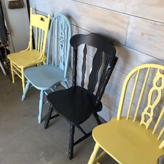 four chairs are lined up against the wall in different colors and styles, one is black, one is yellow