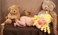 a baby laying on top of a wooden bench next to teddy bears