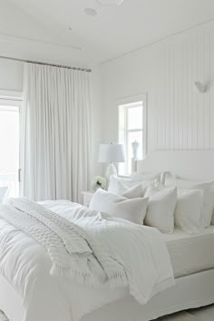 a bedroom with white bedding and curtains