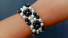 a close up of a person's hand wearing a bracelet with pearls and black beads