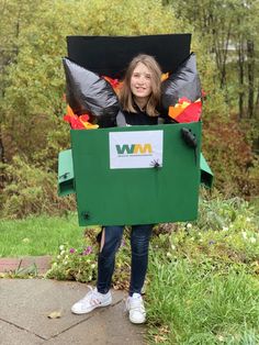 a woman standing in the grass holding up a green box with leaves on it's sides