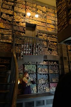 a woman standing in front of a wall filled with boxes and lights next to an escalator