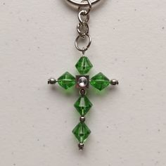 a green cross keychain hanging from a metal ring on a white surface,