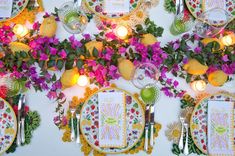 a table topped with lots of plates covered in flowers next to lit candles and fruit