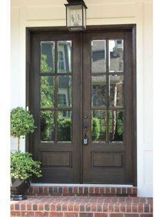 two potted plants sitting on the front steps of a house with double doors and windows