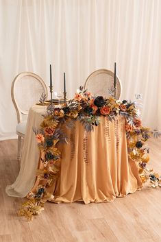 the table is covered with an orange cloth and floral arrangements on it, along with two chairs