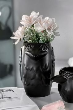 two black vases with flowers in them sitting on a table next to each other