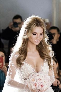 the bride is walking down the runway in her wedding dress and holding a bouquet of flowers