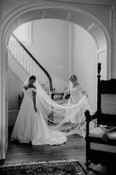 two women standing in front of a staircase with veils over their heads and one woman wearing a wedding dress