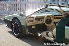 a green and white sports car parked next to a wooden fence with the door open