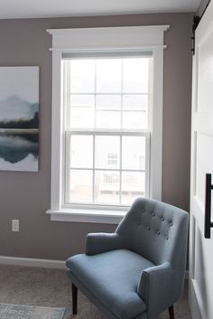 a blue chair sitting in front of a window next to a painting on the wall