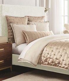 a bed with white and gold comforters in a bedroom next to a window,