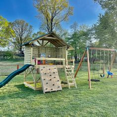 a wooden play set in the grass with a slide and climbing frame next to it