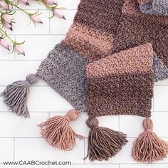 three scarfs with tasselled ends on a white tiled floor next to flowers