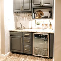 a small kitchen with gray cabinets and white counter tops is pictured in this image, there are wine glasses on the shelves above the sink