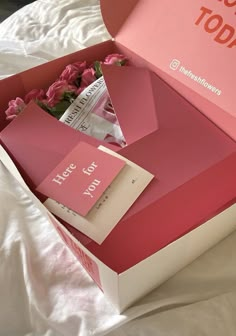 an open pink box with flowers inside on a bed