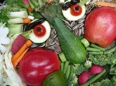 a face made out of fruits and vegetables with eyes on it's head, surrounded by flowers