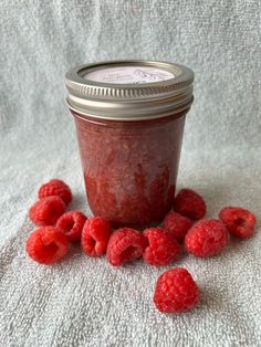 raspberry jam in a glass jar surrounded by fresh raspberries