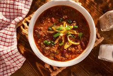 a white bowl filled with chili, cheese and bread on top of a wooden table