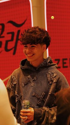 a young man is smiling and holding a drink in his hand while standing next to a coca - cola sign