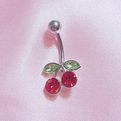 a pair of red and green jeweled navel barbells on a pink background