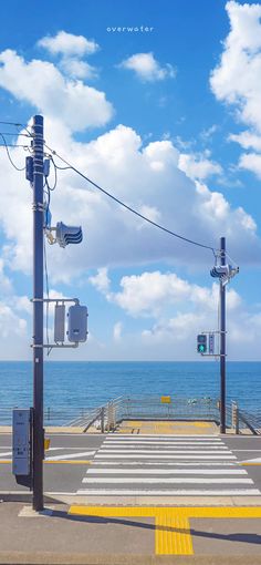 an empty street next to the ocean on a sunny day with blue skies and white clouds