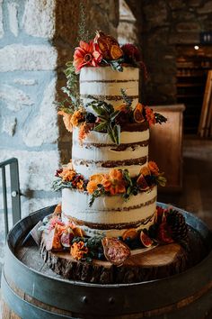 a three tiered cake with orange flowers and greenery sits on top of a barrel