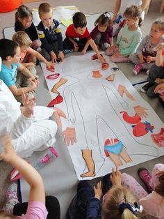 a group of children sitting around a paper cut out of a human body