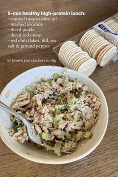 a white bowl filled with chicken salad next to crackers on a wooden counter top