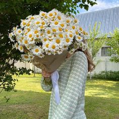 a woman holding a bouquet of daisies in front of her face while standing on the grass