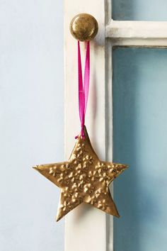 a gold star ornament hanging from the side of a door with a pink ribbon