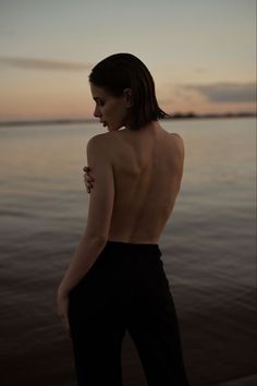 a naked woman standing in front of the ocean at sunset with her back to the camera