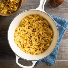 a pan filled with pasta on top of a wooden table next to a bowl of sauce