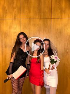 three beautiful women standing next to each other in front of a wooden wall and holding flowers