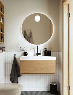 a bathroom with a round mirror above the sink and wooden cabinets on the wall behind it