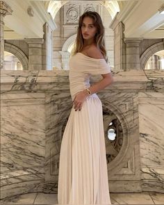 a woman in a long dress standing next to a marble wall and looking at the camera