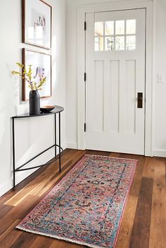 a room with a rug on the floor next to a white door and framed pictures