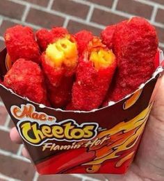 a person holding up a paper container filled with strawberries and cheetos on fire