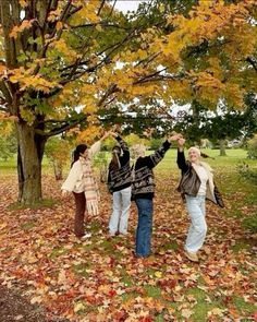 three people standing under a tree with their arms in the air and leaves on the ground