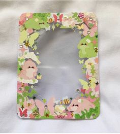 a small mirror with flowers and butterflies on the bottom is sitting on a white sheet