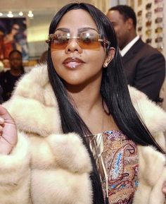 a woman wearing sunglasses and a fur coat is looking at the camera while she holds her hand up