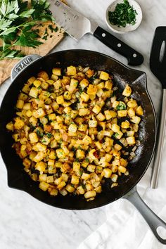 a skillet filled with potatoes on top of a table next to a cutting board