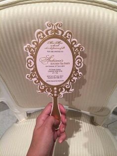 a person holding up a pink and gold wedding card in front of a white chair