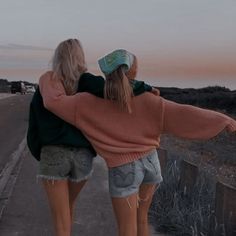 two girls walking down the road with their arms around each other's back,